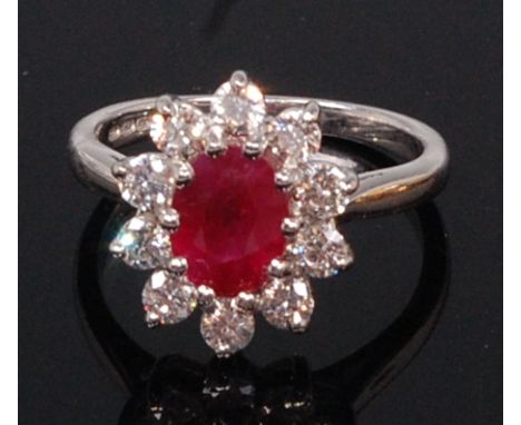 An 18ct white gold, ruby and diamond dress ring, arranged as a flower head cluster, the centre oval cut ruby weighing approx 