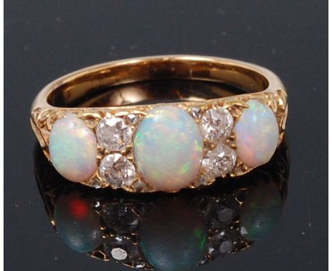 An Edwardian opal and diamond dress ring, arranged as three cabochon opals in a scroll carved setting, the largest weighing 0