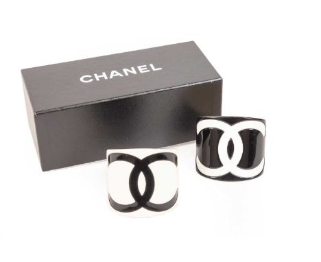 Two Resin Cuff Bracelets, by Chanel, one with a black background and white intertwined 'C's', the other with a white backgrou