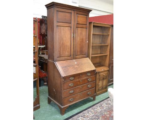 A George III oak bureau cabinet, stepped cornice above a pair of panelled doors enclosing adjustable shelves, fall front encl