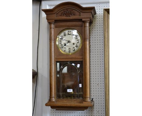 A 1920s light oak wall clock arched pediment, twin winding holes, Arabic numerals, arched fielded bevelled clear glass door, 