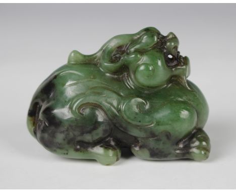 A Chinese green jade carving, modelled as a crouching Buddhistic lion, the stone of mottled green tone with black inclusions,