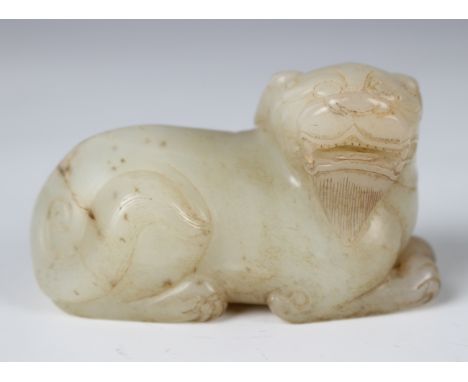 A Chinese pale celadon jade figure of a Buddhistic lion dog, Ming dynasty style but later, modelled in a recumbent pose with 