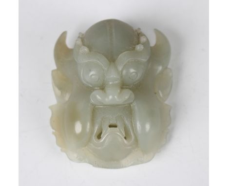 A Chinese pale celadon jade mask buckle/pendant, 20th century, carved with a horned grotesque, length 5cm. Provenance: from t