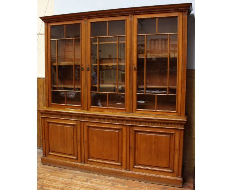 An Edwardian light oak triple bookcase, with ogee moulded cornice, and dentil moulding above three lattice-glazed doors enclo