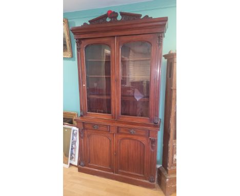 An Edwardian mahogany cabinet bookcase having carved pediment over twin glazed doors opening to four adjustable shelves, the 