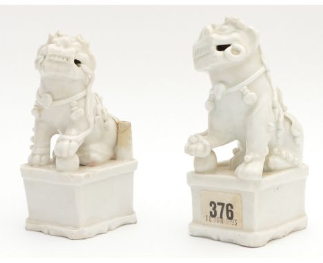 A pair of Chinese blanc de chine porcelain figures of a Dog of Fo, modelled seated with one paw resting on a ball, raised on 