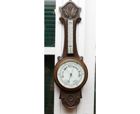An early 20th century wall barometer, having ceramic circular dial below thermometer in carved oak case, 81cm long.