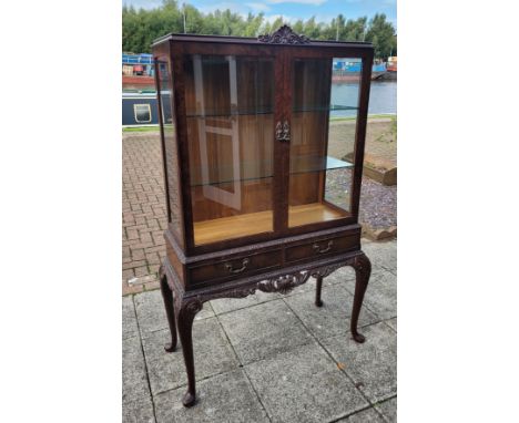 An Edwardian walnut display cabinet, the glazed doors opening to fitted glass shelves over two frieze drawers, carved cabriol