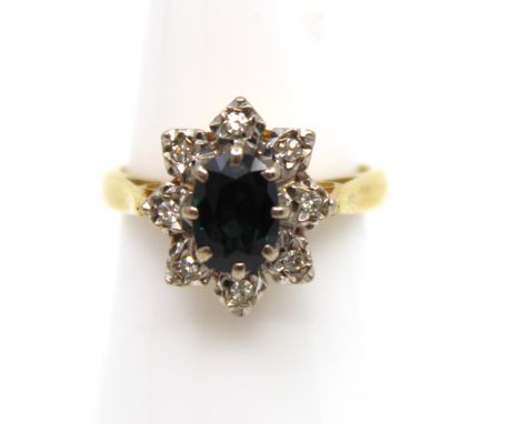 18ct Yellow Gold Sapphire and Diamond Cluster Ring  The ring contains an Oval Brilliant Cut Inky Blue Sapphire that measures 