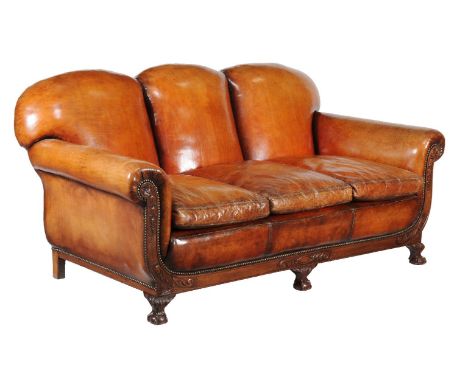 A carved mahogany and leather upholstered sofa, circa 1930, the triple padded back and triple loose cushion seat flanked by s