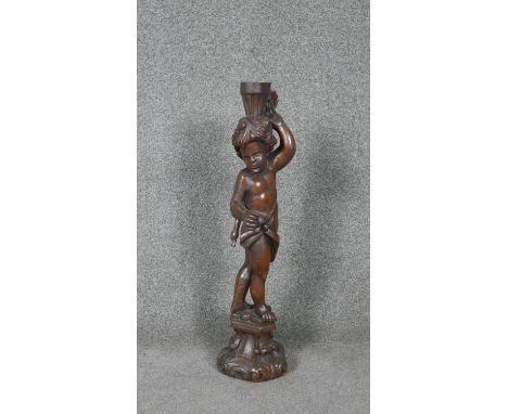A carved candlestick in the form of a cherub on a Rococo socle. 