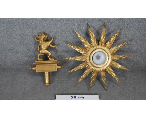 A gilded metal sunburst wall lamp along with a carved gilded wooden rampant lion finial. 
