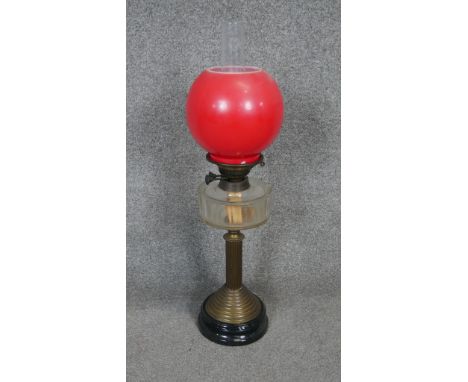 A Victorian brass oil lamp with black base and red opaque glass ball shade and glass oil well. 