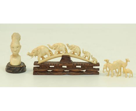A collection of ivory carvings comprising a carved head on wooden plinth, an elephant bridge on wooden stand and four carved 
