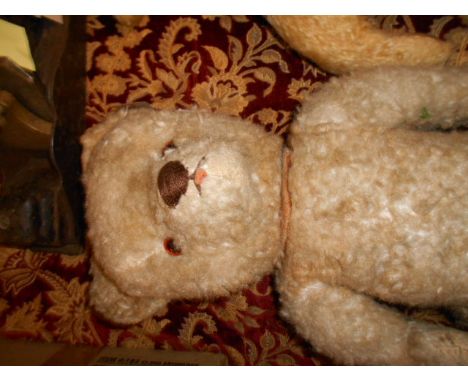 A vintage straw filled teddy bear with pale fur, articulated limbs and glass eyes