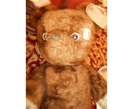 A vintage straw filled teddy bear with dark brown fur, articulated limbs and ceramic eyes