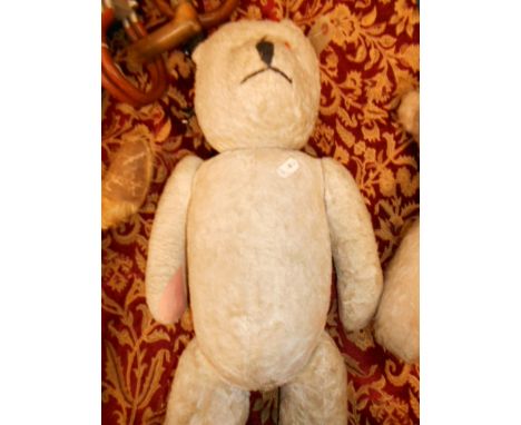 A vintage straw filled teddy bear with pale fur, articulated limbs and one glass eye