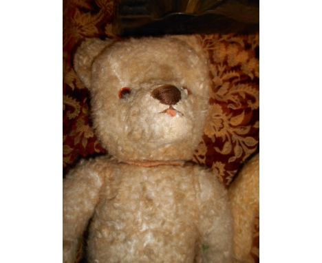 A vintage straw filled teddy bear with light tan fur, articulated limbs and ceramic eyes