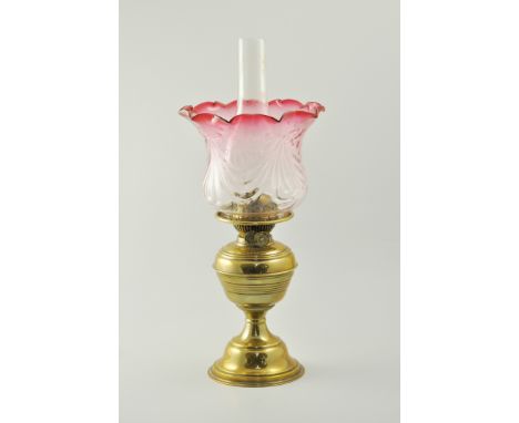 Brass oil lamp, ruby tinted and wrythen moulded shade, with chimney, height overall 49cm.