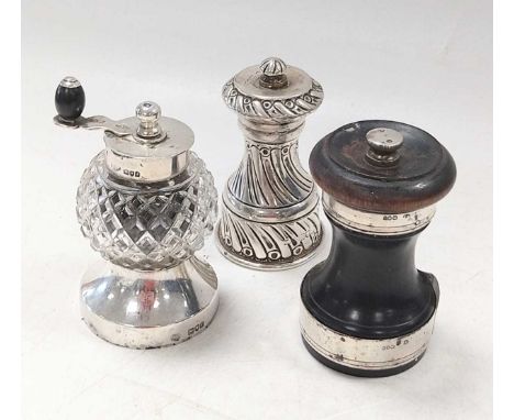 A trio of silver pepper grinders; the first of traditional capstan form, the second with glass reservoir, the third of wooden