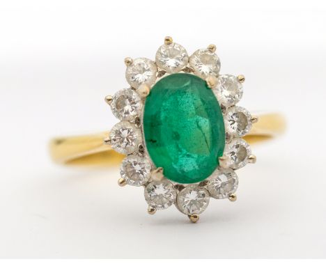 An emerald and diamond 18ct gold cluster ring, comprising a central oval mixed cut emerald, approx 6 x 8mm, within a border o