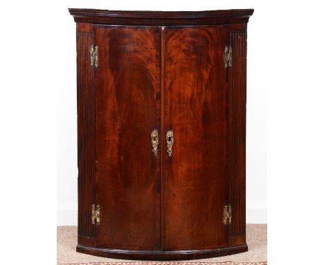 A George III mahogany hanging corner cupboard, the cavetto cornice above figured doors with brass escutcheons and H-hinges be