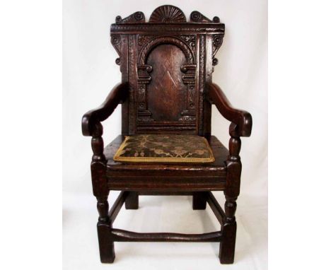 A 17th century oak Wainscot Armchair, the crest rail with broken arch centred with a sunburst, carved panel back with feature