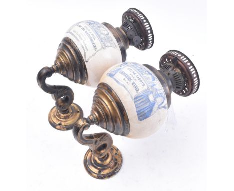 A pair of early 20th century point of sale advertising brass wall oil lamp sconces. Each lamp having a bulbous ceramic wells 
