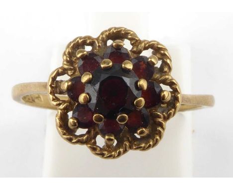 A 9ct rose gold ruby ring, the central claw set cut ruby within a border of eight tiny rubies, in a rope twist flower head de