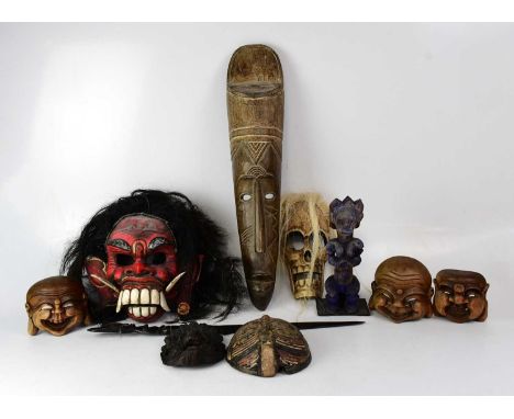 Various African tribal masks to include a red painted example with faux hair, a skull and various other smaller models and a 