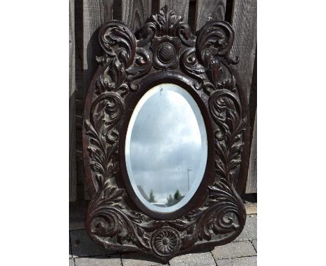 A wall-mounted oval bevel edged mirror, 44 x 28cm, mounted in a late 17th/early 18th century carved oak frame, with pineapple