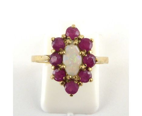 A 9ct gold opal and ruby cluster ring, the central claw set white opal with flashes of green, within a border of eight claw s