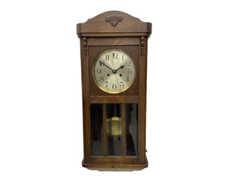 A 1930’s wall clock in an oak case with a full-length door, three glazed panels and visible pendulum, case with a shaped pedi