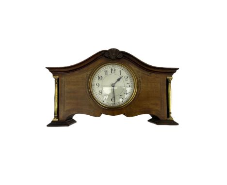 An Edwardian mantle clock in a mahogany case with a serpentine pediment and recessed brass pillars, 3-1/2” white dial, uprigh