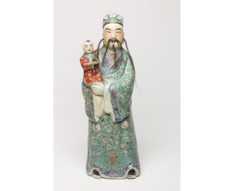 A LARGE CHINESE PORCELAIN FIGURE, modelled as a man with horse hair beard and moustache, wearing a famille rose robe and hold