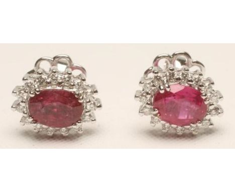 A PAIR OF RUBY AND DIAMOND CLUSTER EAR STUDS, the oval cut rubies claw set to a border of prong set small diamonds to white m