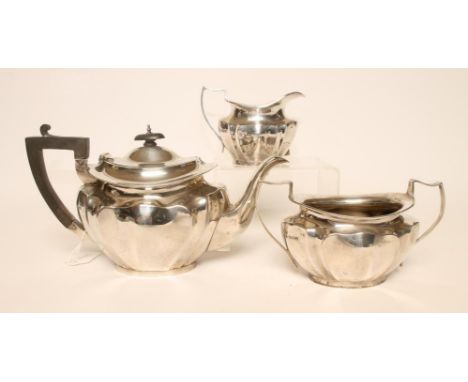 A SILVER THREE PIECE TEA SERVICE, makers Deakin & Deakin, Sheffield 1926, of lobed oval form, comprising teapot with swept sh