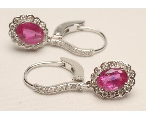 A PAIR OF RUBY AND DIAMOND CLUSTER EARRINGS, the oval facet cut rubies claw set to a border of fourteen round brilliant cut d