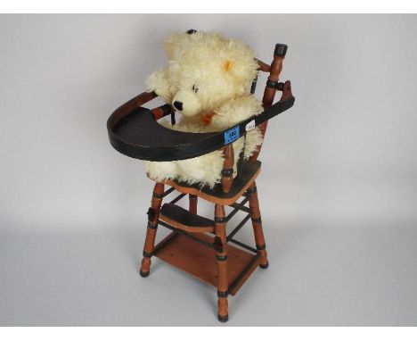 Steiff - A Steiff teddy bear with button and yellow tag in ear, displayed in a metamorphic high chair. Item appears to be in 