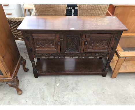 A HEAVILY CARVED OAK CABINET WITH TWO DOORS AND LOWER SHELF 