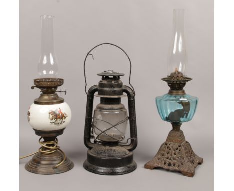 A Victorian cast iron oil lamp with blue glass font along with a later lamp altered to electric and a vintage storm lantern.