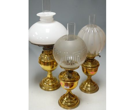 An early 20th century brass pedestal oil lamp having melon shaped clear glass globular shade together with two others similar