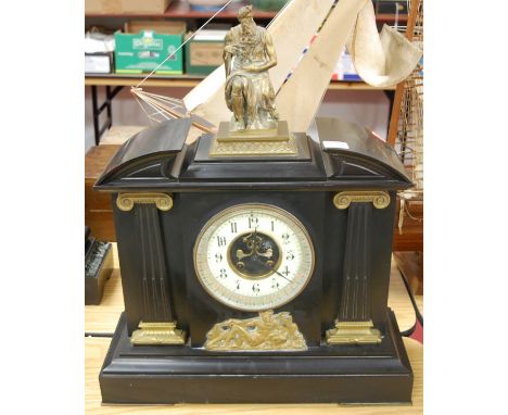 A late Victorian slate mantel clock of architectural form, with enamel dial and Arabic numerals, surmounted by a seated figur