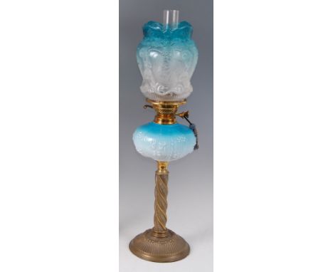 An Art Nouveau brass and blue glass pedestal oil lamp, having a frosted blue glass tinted shade, with all-over raised stylise