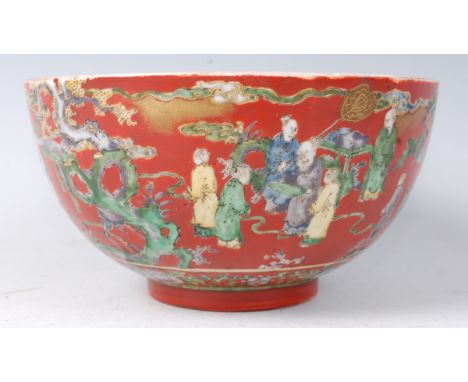 A Japanese Kutani bowl in the Mobukei style, enamel decorated with figure landscape scenes on a coral red ground, heightened 
