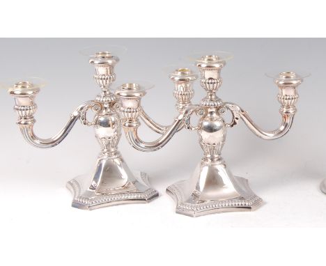 A pair of sterling silver three light candelabra, having half-reeded urn shaped nozzles to a quatraform base, gross weight 42