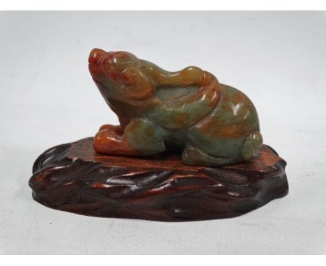 A Chinese green and russet jade carving of a recumbant mythical beast, upon wooden stand, length 5cm.
