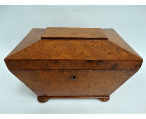 An early 19th century burr elm veneered tea caddy of sarcophagus form, hinged to reveal two lidded compartments and raised on