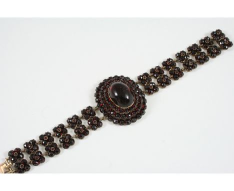 A VICTORIAN GARNET BRACELET the central oval garnet cabochon is set within a triple surround of faceted circular garnets, wit